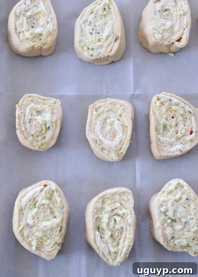 Uncooked creamy pickle rolls arranged neatly, cut side up, on a parchment-lined baking sheet before baking.