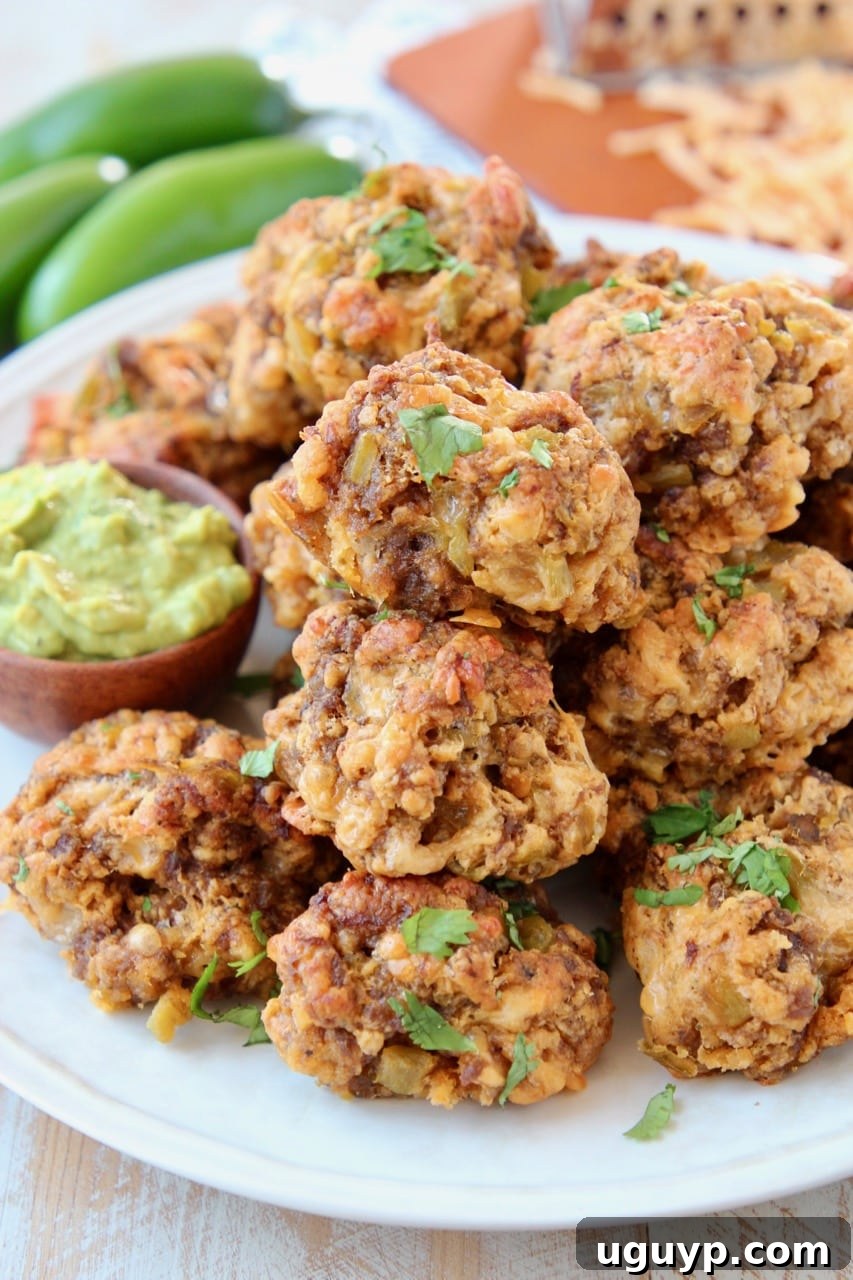 Sausage balls piled up on a plate with a small bowl of avocado dipping sauce, garnished with fresh cilantro.