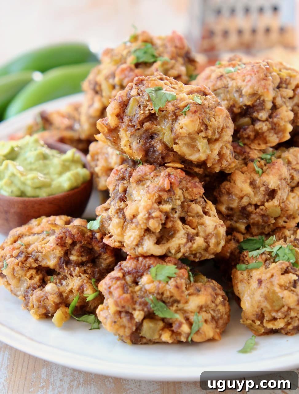 Chorizo sausage balls piled on a plate with avocado sauce in a small wooden bowl, ready to be served.