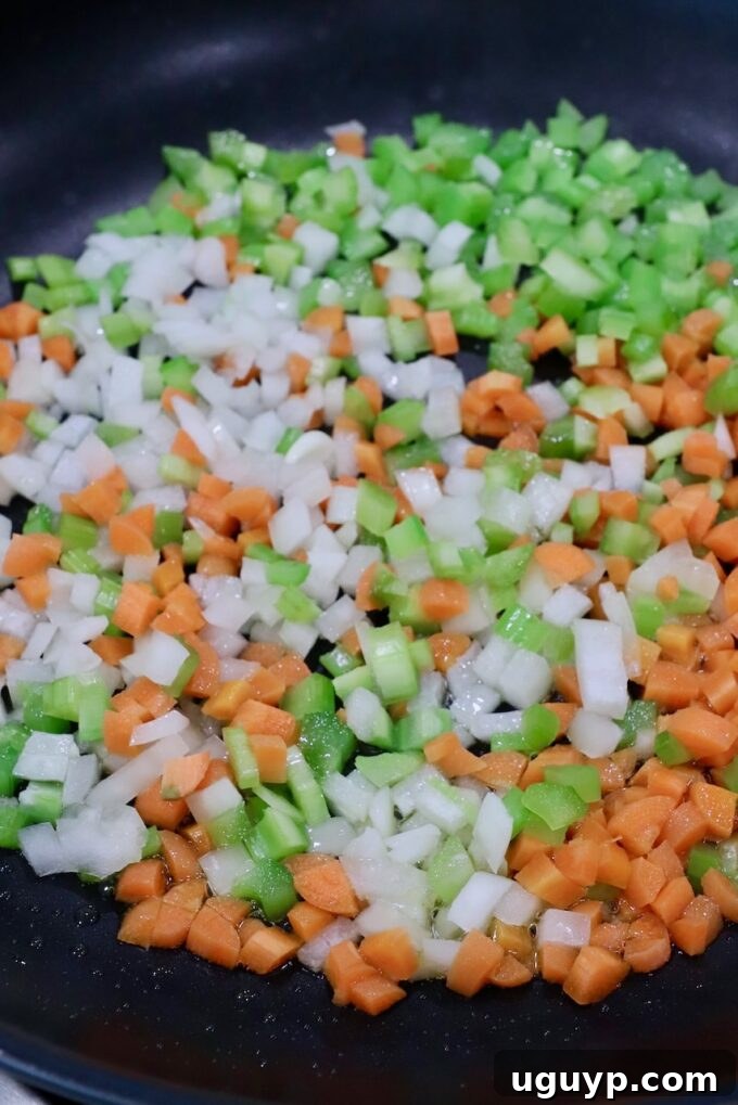 Finely diced onions, carrots, and celery cooking in a skillet with olive oil, softening for the meatball mixture.