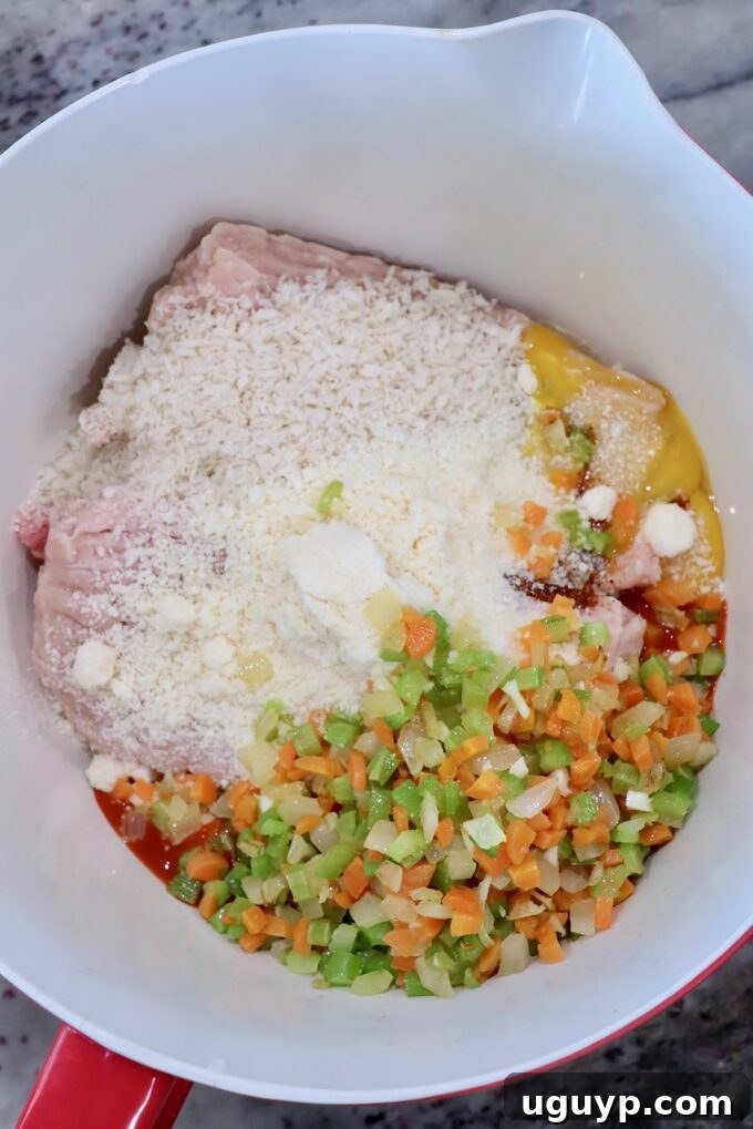 All the essential ingredients for buffalo chicken meatballs, including ground chicken and pork, seasonings, and cooked vegetables, gathered in a large mixing bowl.