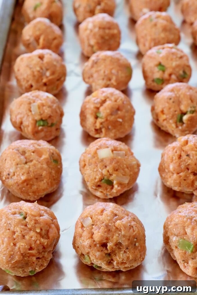 Uniformly shaped uncooked buffalo chicken meatballs neatly arranged in a single layer on a foil-lined baking sheet, prepared for broiling.