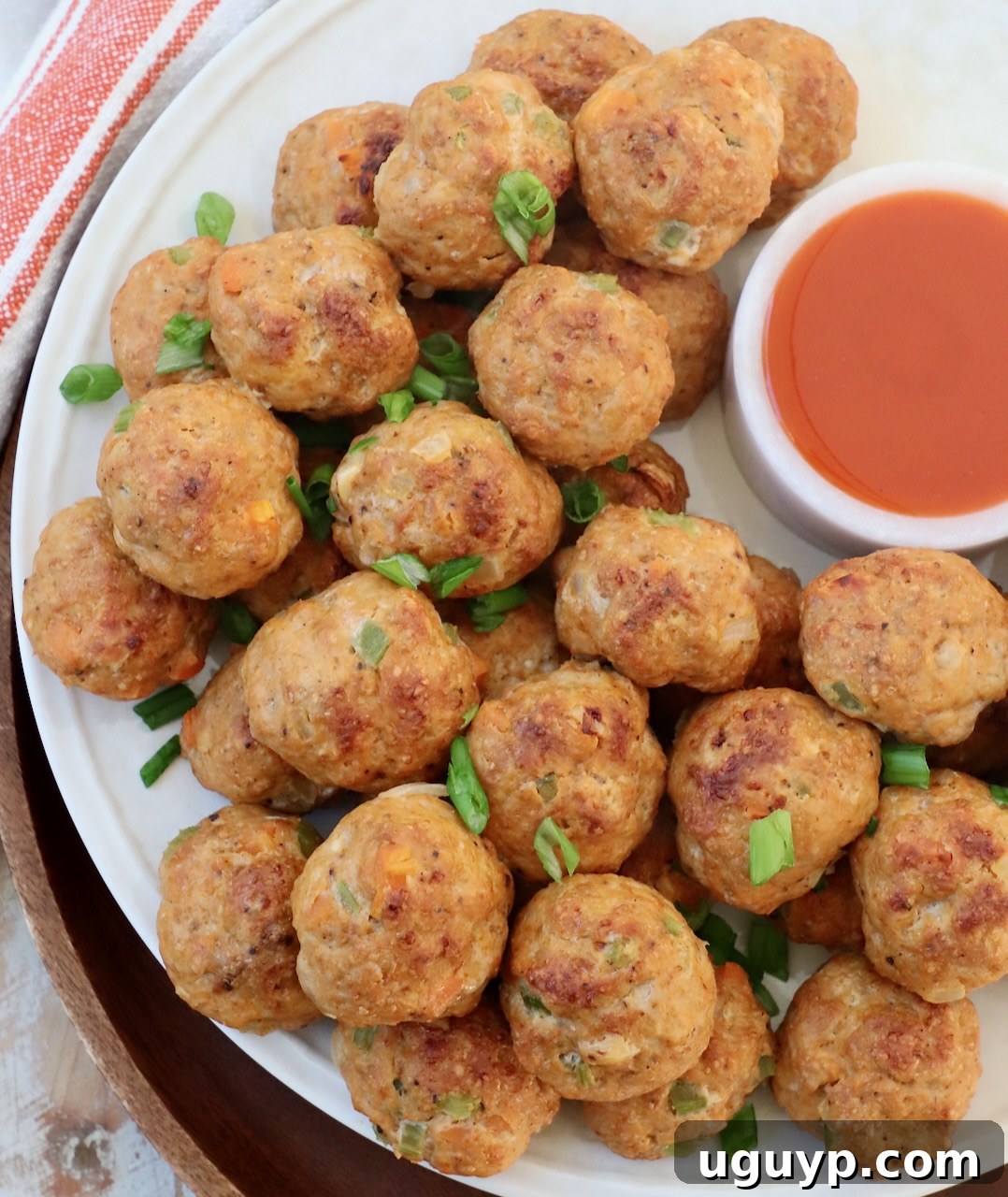 Perfectly cooked buffalo chicken meatballs arranged on a white plate, accompanied by a small serving of buffalo sauce for dipping.