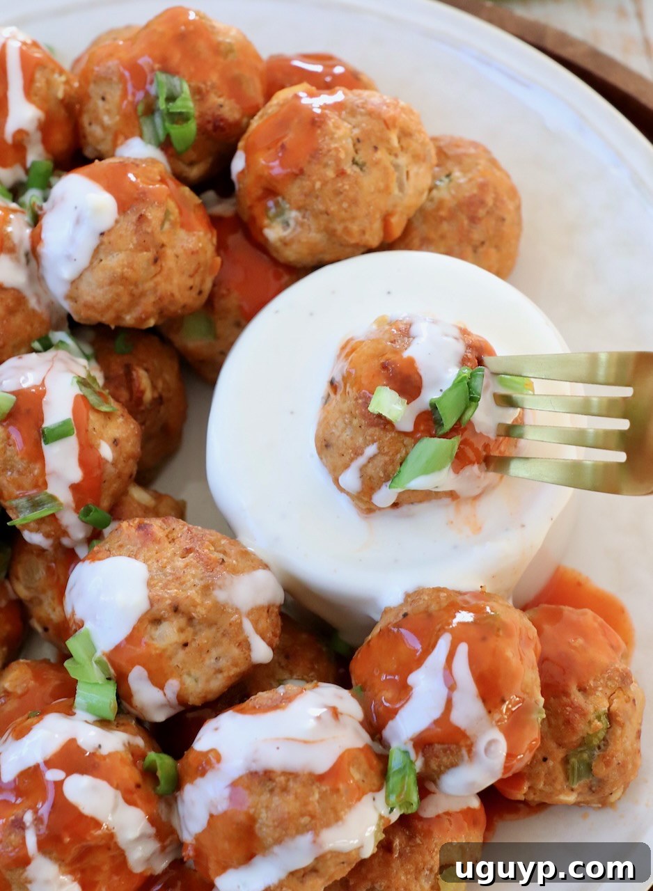 A perfectly cooked buffalo chicken meatball impaled on a fork, poised above a bowl of rich, creamy blue cheese dressing, ready for dipping.