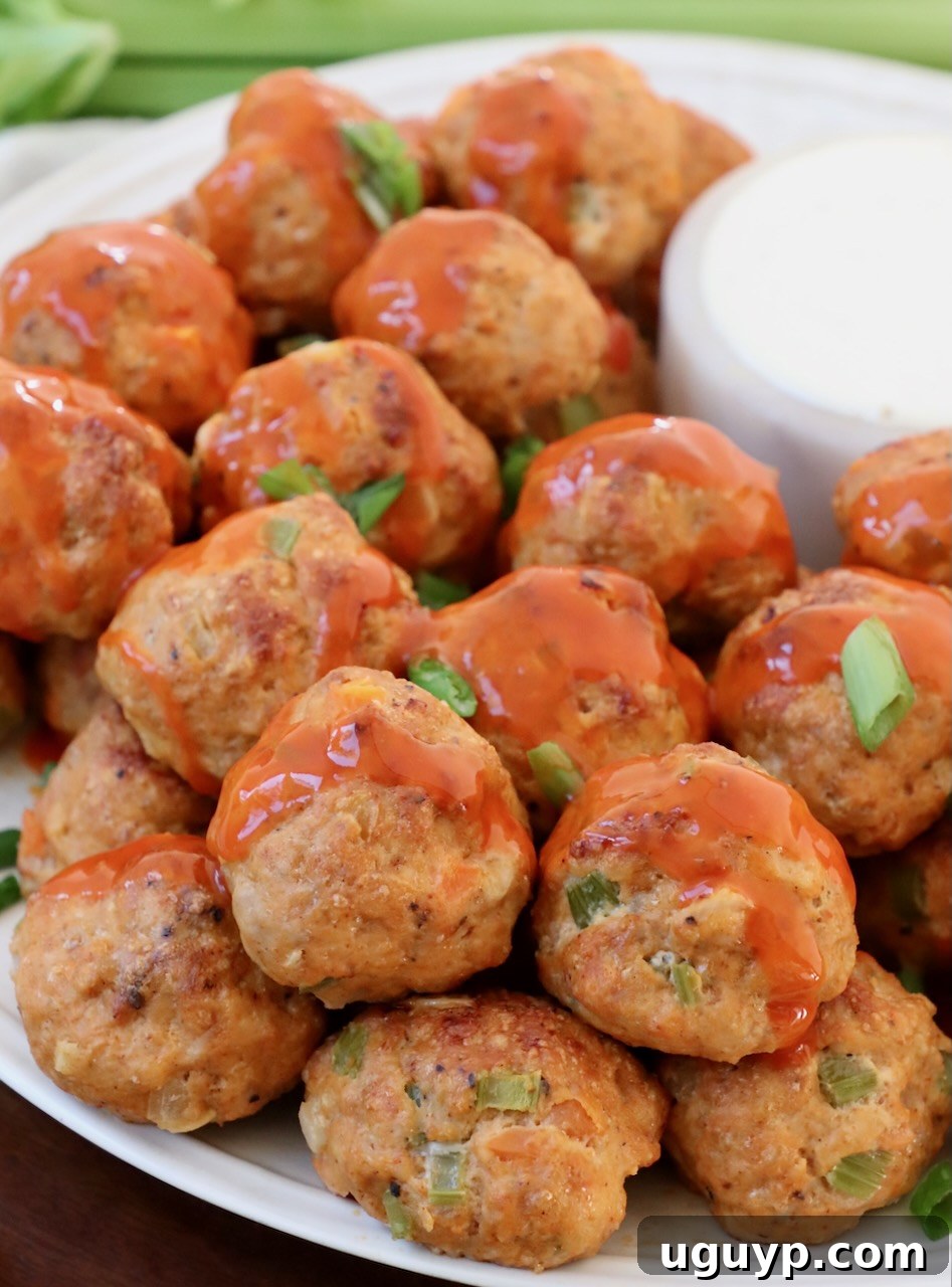 Close-up photograph of buffalo chicken meatballs artfully arranged on a plate, generously coated and drizzled with a vibrant buffalo sauce, showcasing their irresistible appeal.