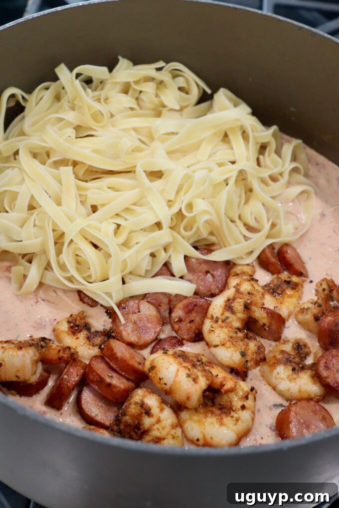 Cooked pasta, shrimp, and sausage added to Cajun Alfredo sauce in a pan