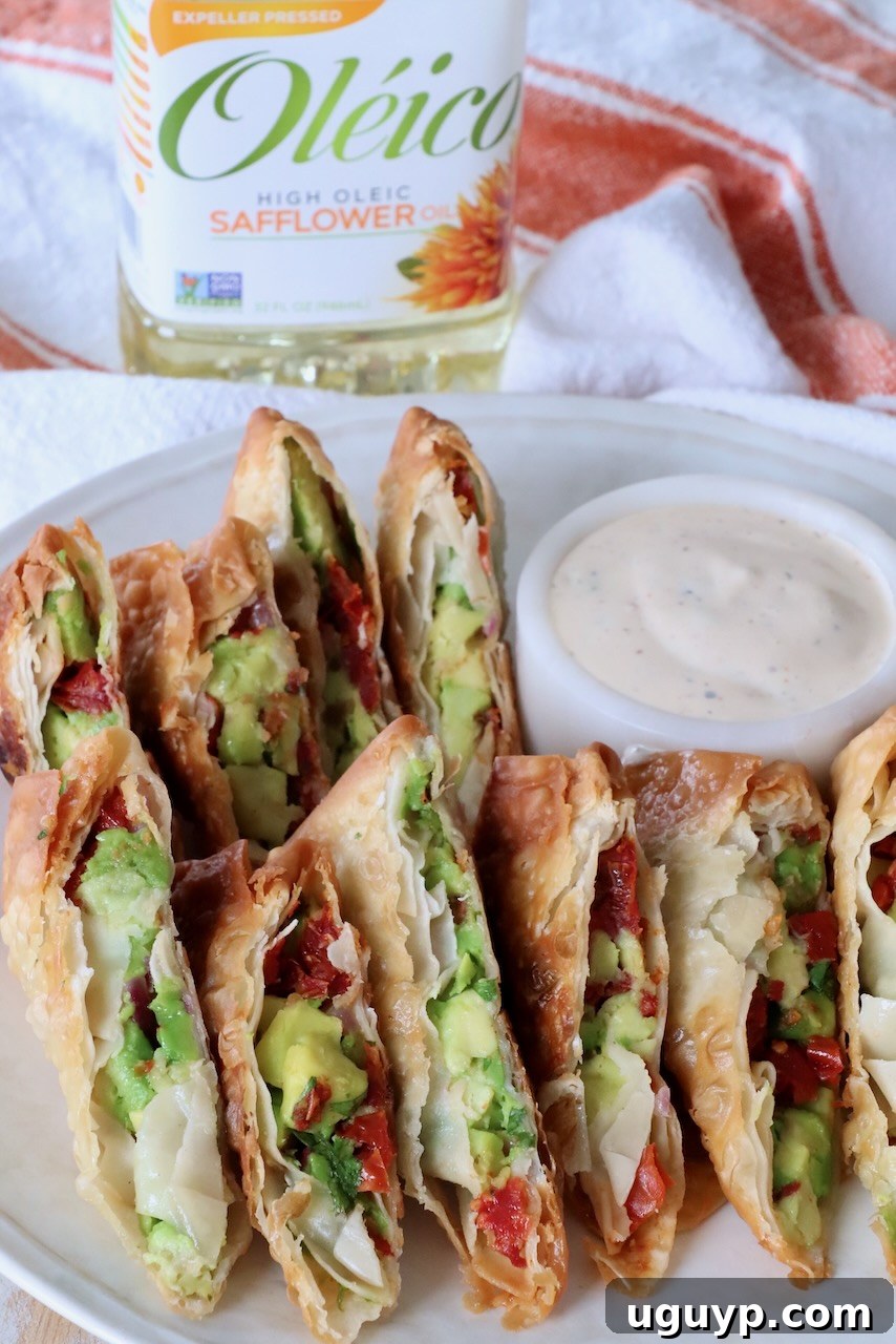 Crispy avocado egg rolls sliced in half, revealing their vibrant green filling, served on a plate with a small bowl of ranch dressing.