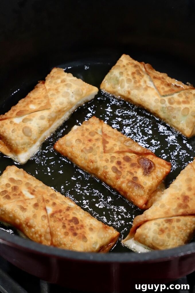 A batch of avocado egg rolls frying evenly in a pan, showcasing their beautiful golden-brown color developing in the hot oil.