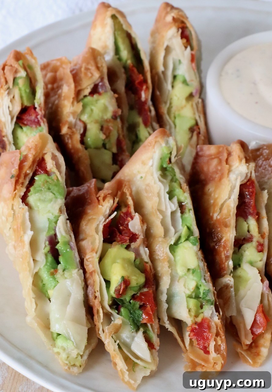 Crispy avocado egg rolls, freshly fried and sliced in half to reveal the creamy green filling, artfully arranged on a white plate.