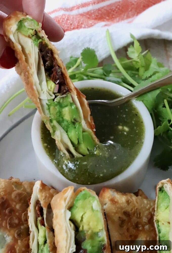 A close-up shot of a crispy avocado egg roll being dipped into a luscious tamarind cashew dipping sauce, highlighting the perfect pairing.