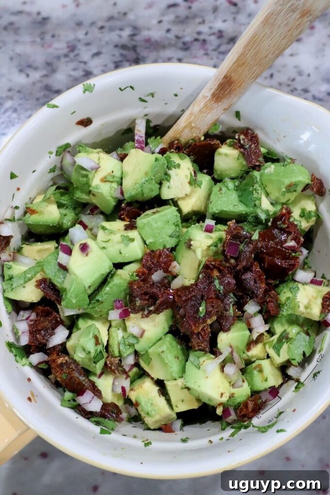 A close-up of the avocado egg roll filling after being gently mixed, showcasing the vibrant green avocado, red sun-dried tomatoes, and fresh herbs.