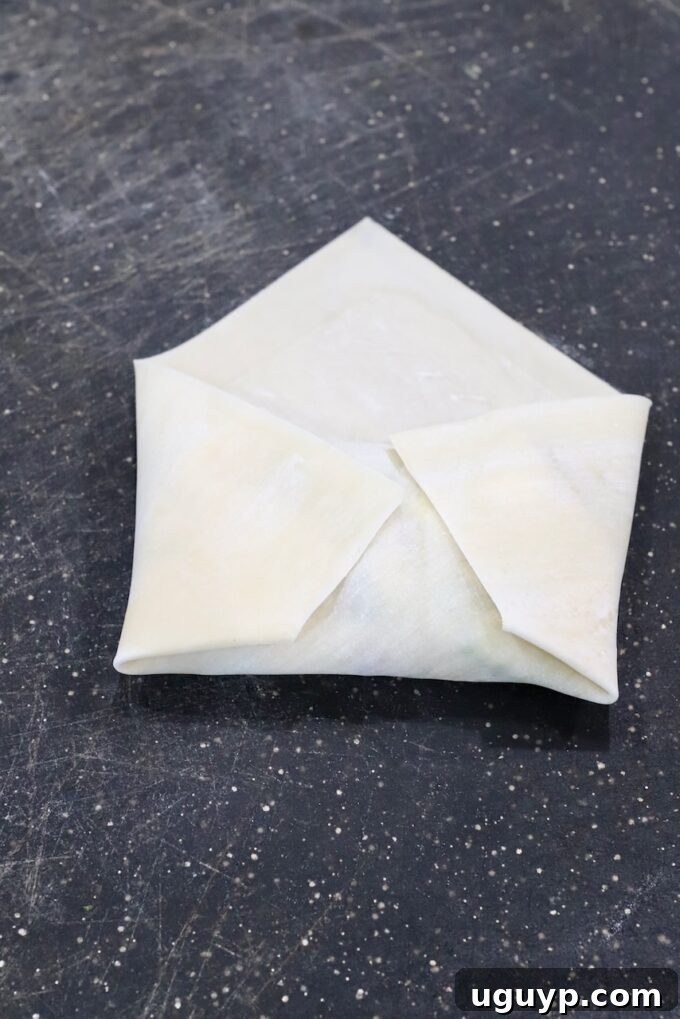 The sides of the egg roll wrapper folded inward over the central filling, preparing for the final roll to seal the ingredients.