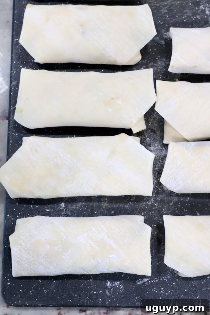 Several uncooked, tightly rolled egg rolls neatly arranged on a cutting board, waiting to be fried.