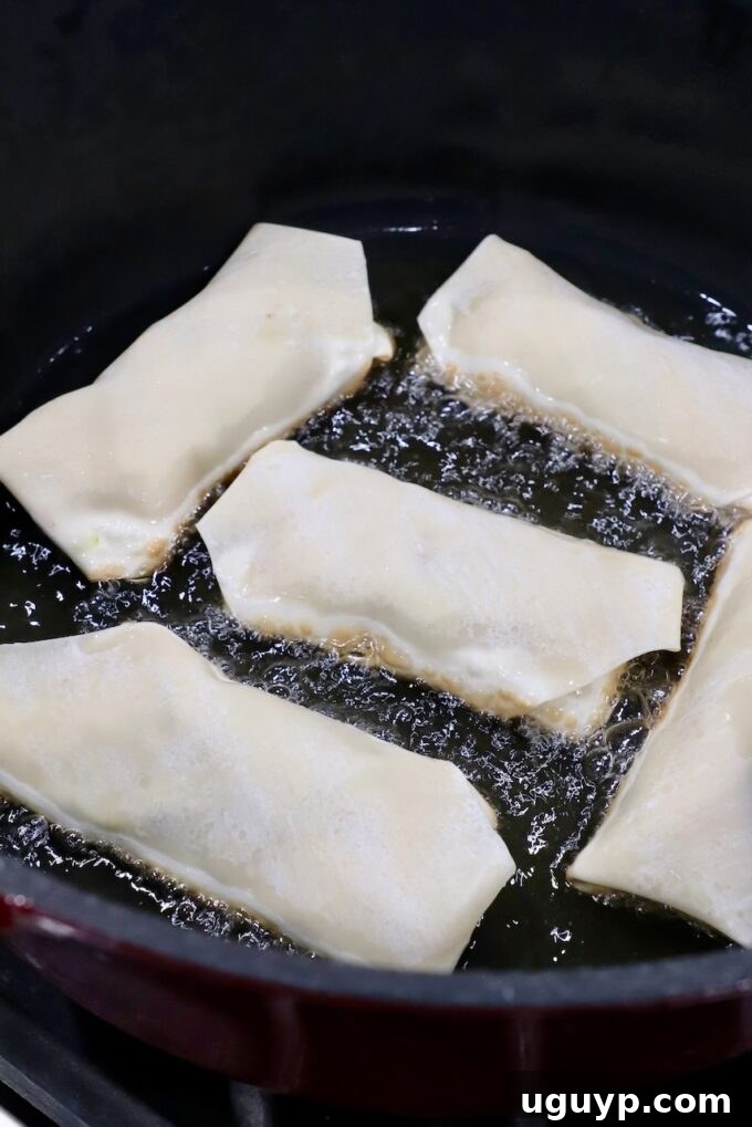 Avocado egg rolls sizzling in hot Oléico Safflower Oil within a large skillet, beginning to turn golden brown.