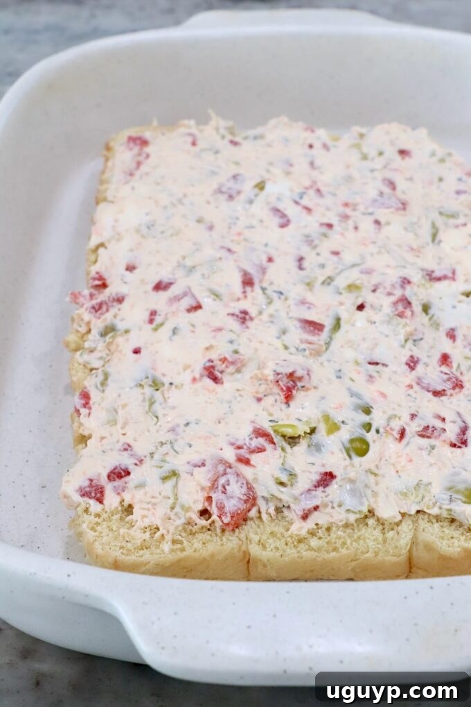 Bottom half of rolls topped with seasoned cream cheese in a casserole dish