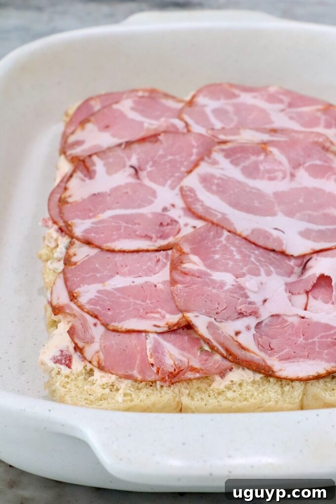 Rolls topped with cream cheese and capocollo in a casserole dish