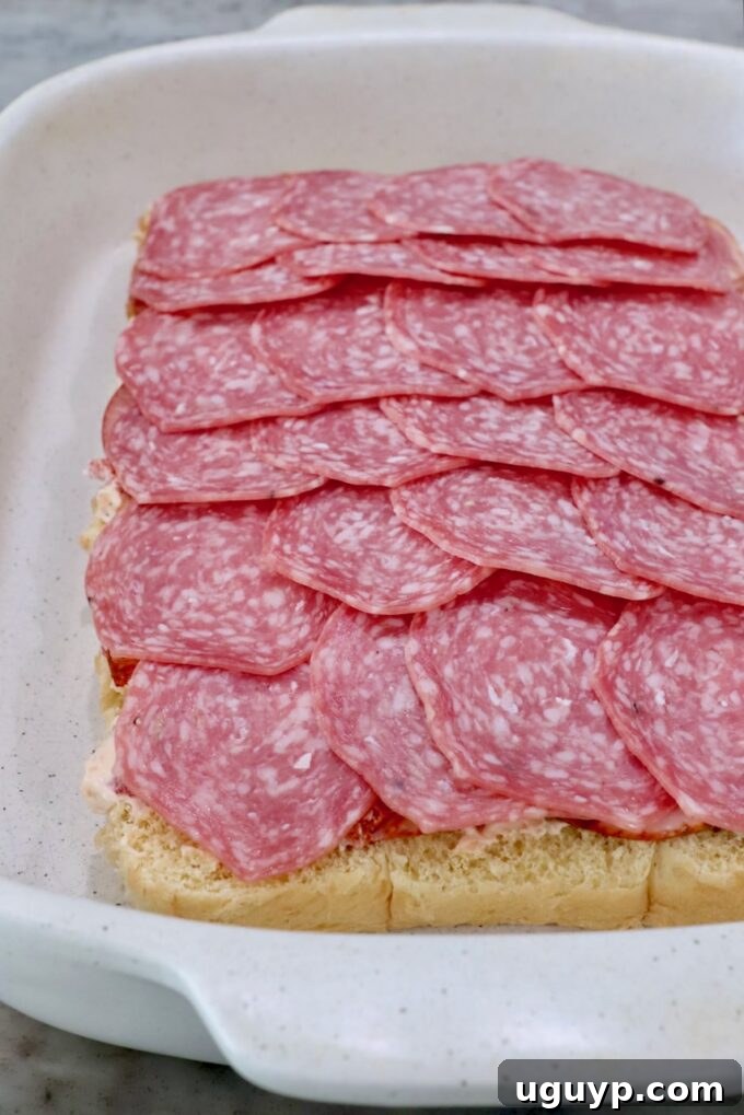 Rolls topped with cream cheese and salami in a casserole dish