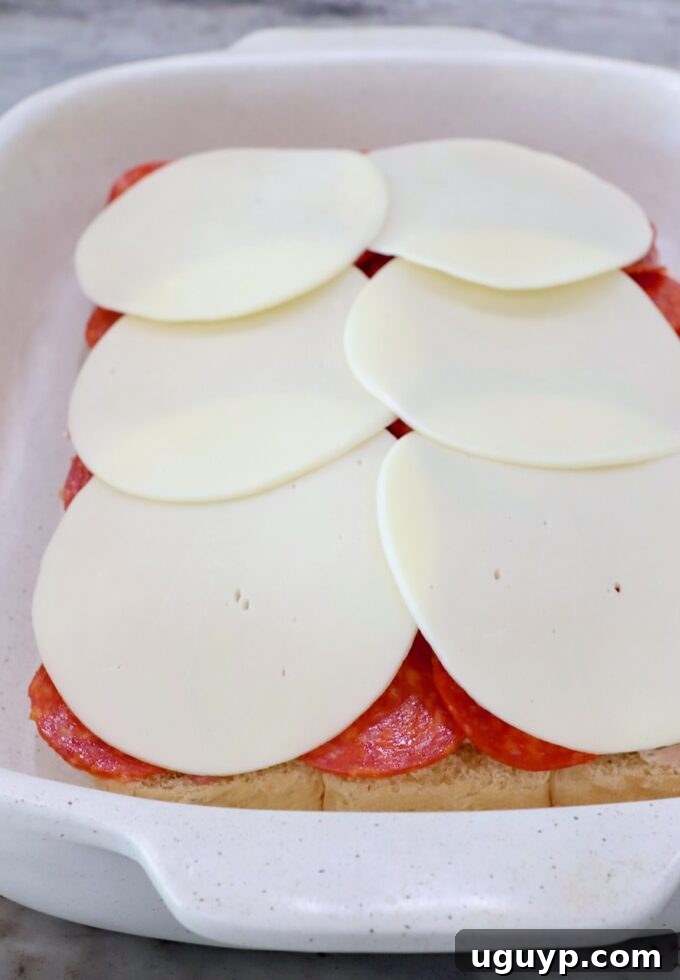 Rolls topped with cream cheese, sliced deli meat, and provolone cheese in a casserole dish