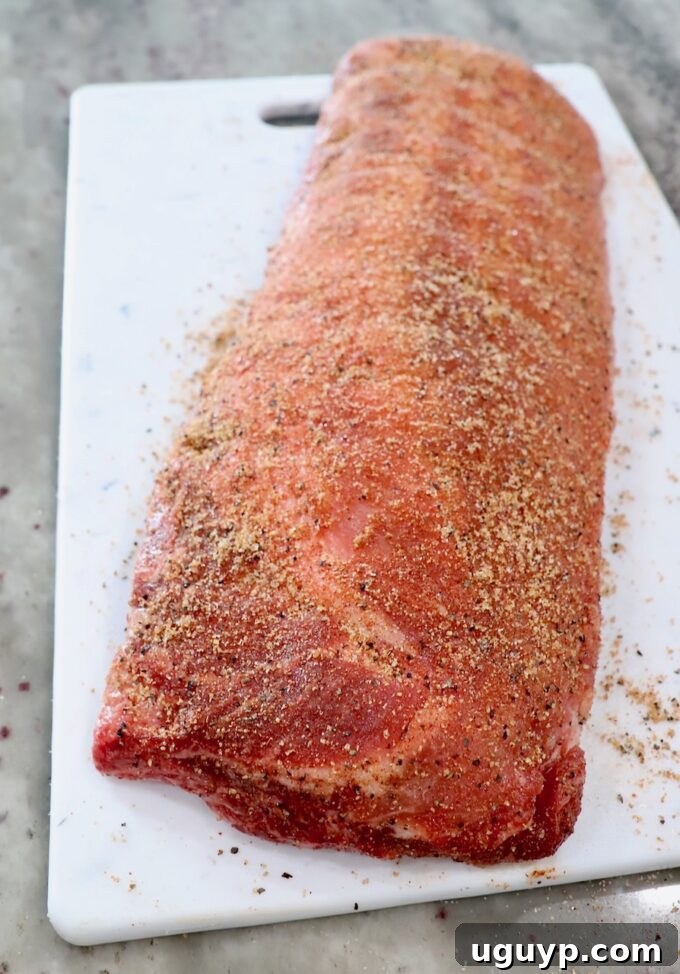 Seasoned rack of baby back ribs resting on a white cutting board, covered with dry rub.