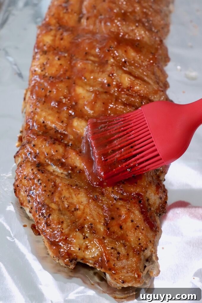Cooked rack of ribs on a foil-lined baking sheet, freshly brushed with BBQ sauce and ready for broiling.