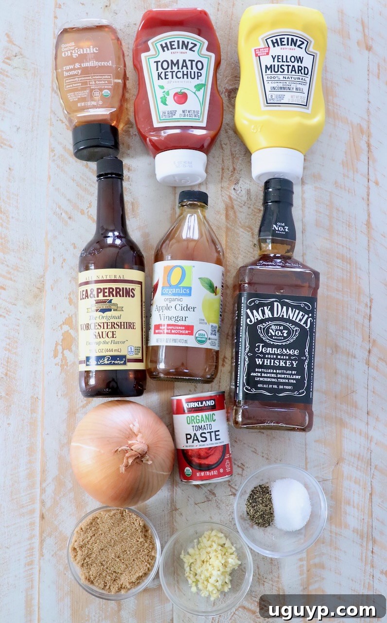 All the fresh ingredients for homemade Jack Daniel's BBQ sauce, including a yellow onion, garlic cloves, ketchup, honey, brown sugar, and a bottle of whiskey, are neatly arranged on a white wooden board, ready for preparation.