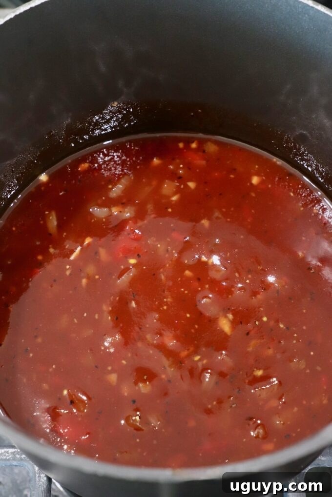 A rich, dark Jack Daniel's BBQ sauce bubbling gently in a saucepan on the stove, showing its glossy, thickening consistency as it simmers to perfection.