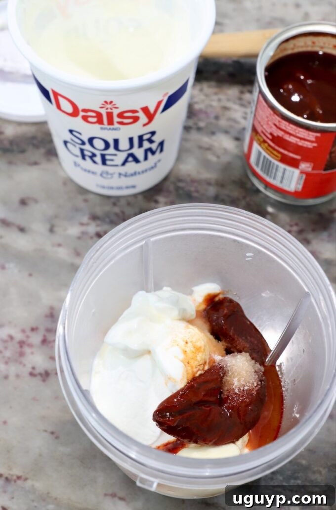 chipotle peppers and sour cream being added to a blender cup