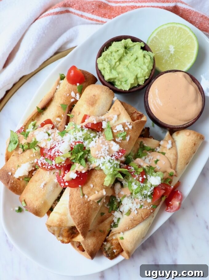 crispy chicken taquitos stacked on a plate with diced tomatoes and cotija cheese