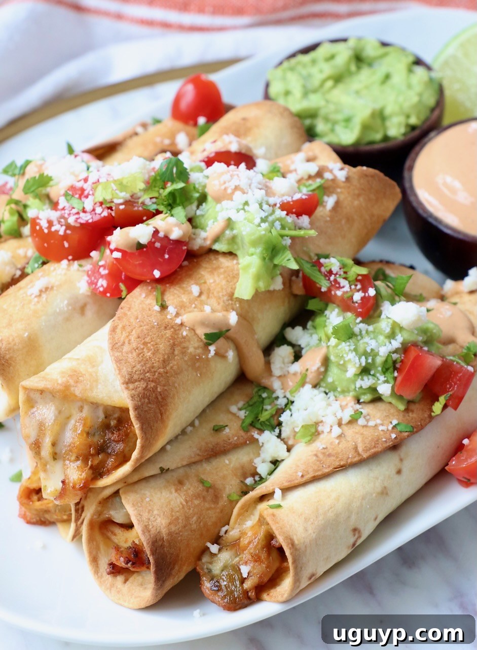 cooked taquitos stacked up on plate, topped with diced tomatoes, cilantro and cotija cheese