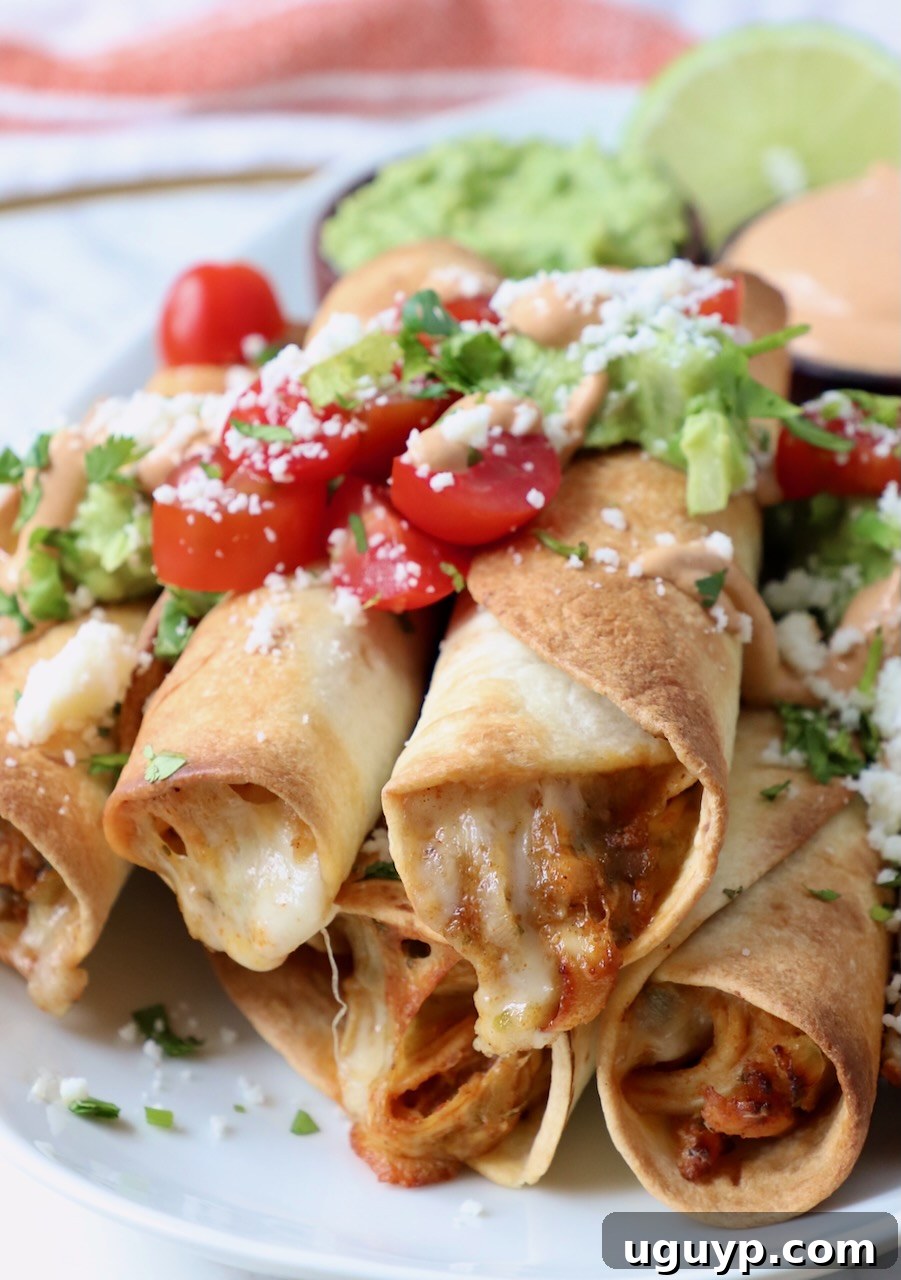 taquitos stacked up on a plate topped with guacamole and diced tomatoes