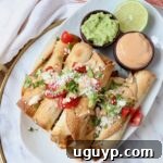 cooked taquitos stacked up on plate with guacamole and chipotle sauce