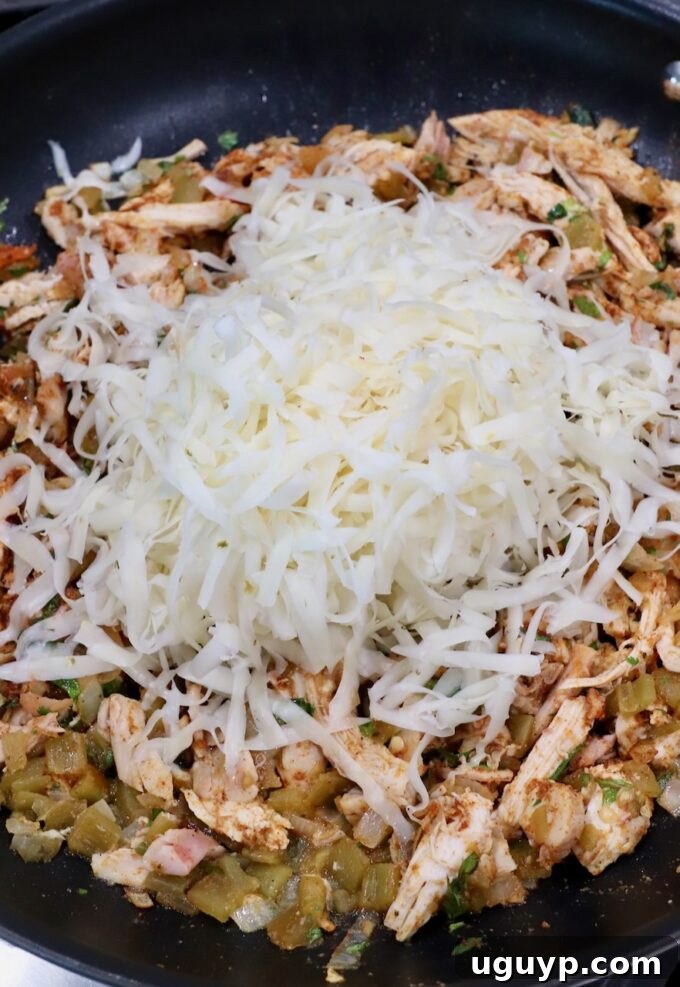 seasoned shredded chicken in skillet topped with shredded pepper jack cheese