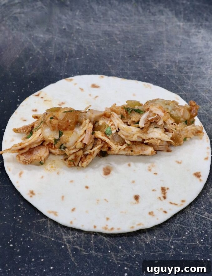 seasoned shredded chicken and cheese in the middle of a tortilla on a cutting board