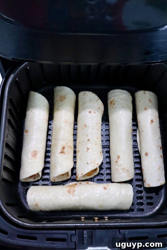 uncooked taquitos in an air fryer basket