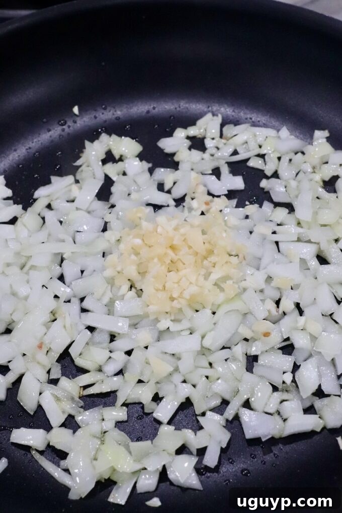Diced yellow onions and minced garlic gently sautéing in a skillet, creating an aromatic base for the Crock Pot Meatloaf.