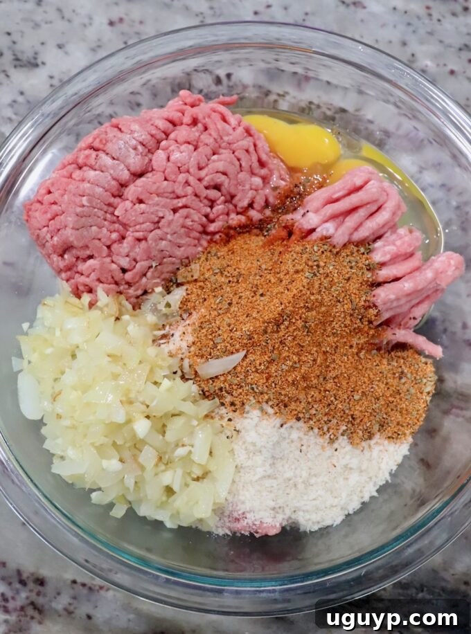 A large mixing bowl containing ground pork and beef, eggs, spices, cooked onions, and breadcrumbs, ready to be combined for the meatloaf mixture.