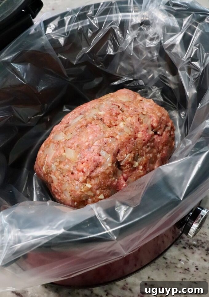 Uncooked meatloaf, perfectly formed and placed within a slow cooker lined for easy cleanup, awaiting its long, slow cooking process.