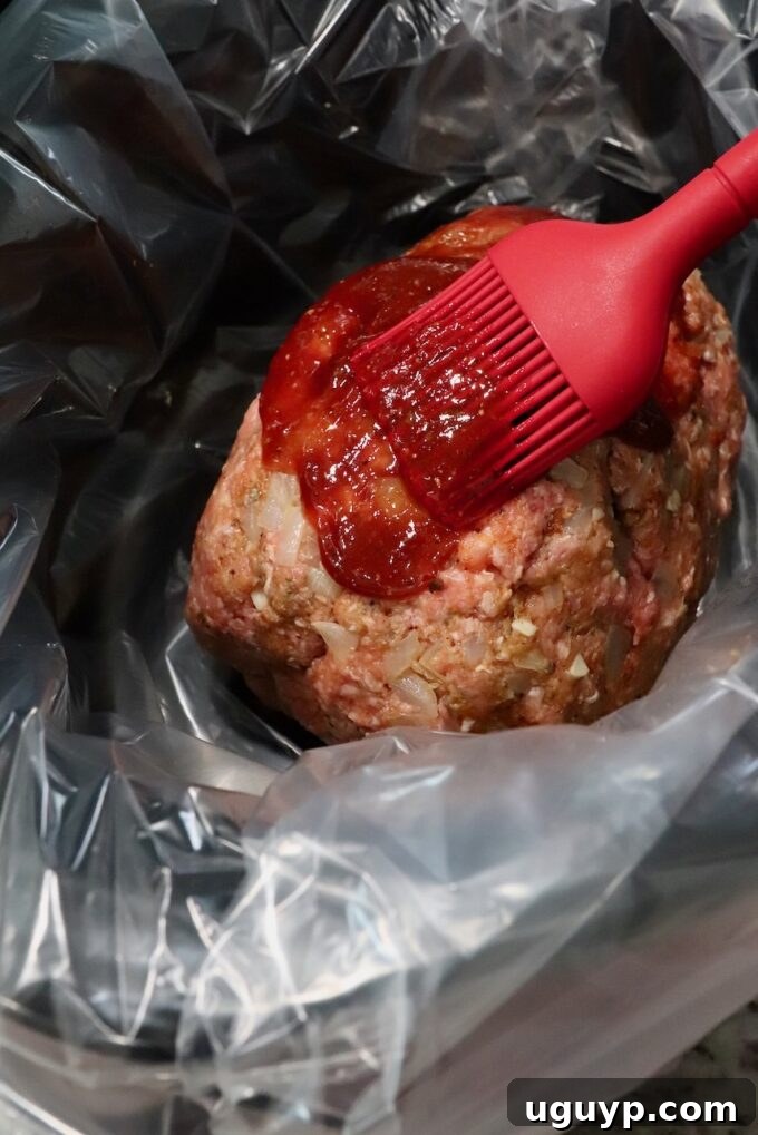 Raw meatloaf in the slow cooker, glistening with a freshly brushed layer of sweet and savory glaze, ready for cooking.
