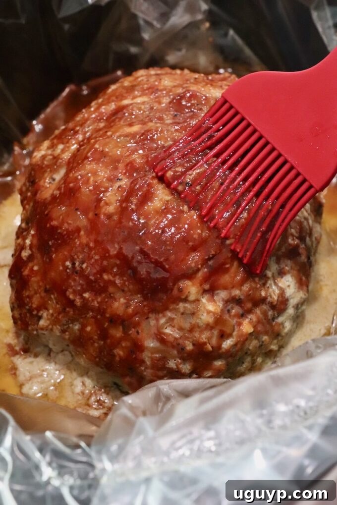 A perfectly cooked, glazed meatloaf resting in the slow cooker, its rich brown surface invitingly brushed with a final layer of sauce.