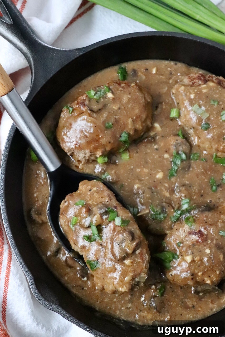 salisbury steak with mushroom gravy in skillet with serving spoon