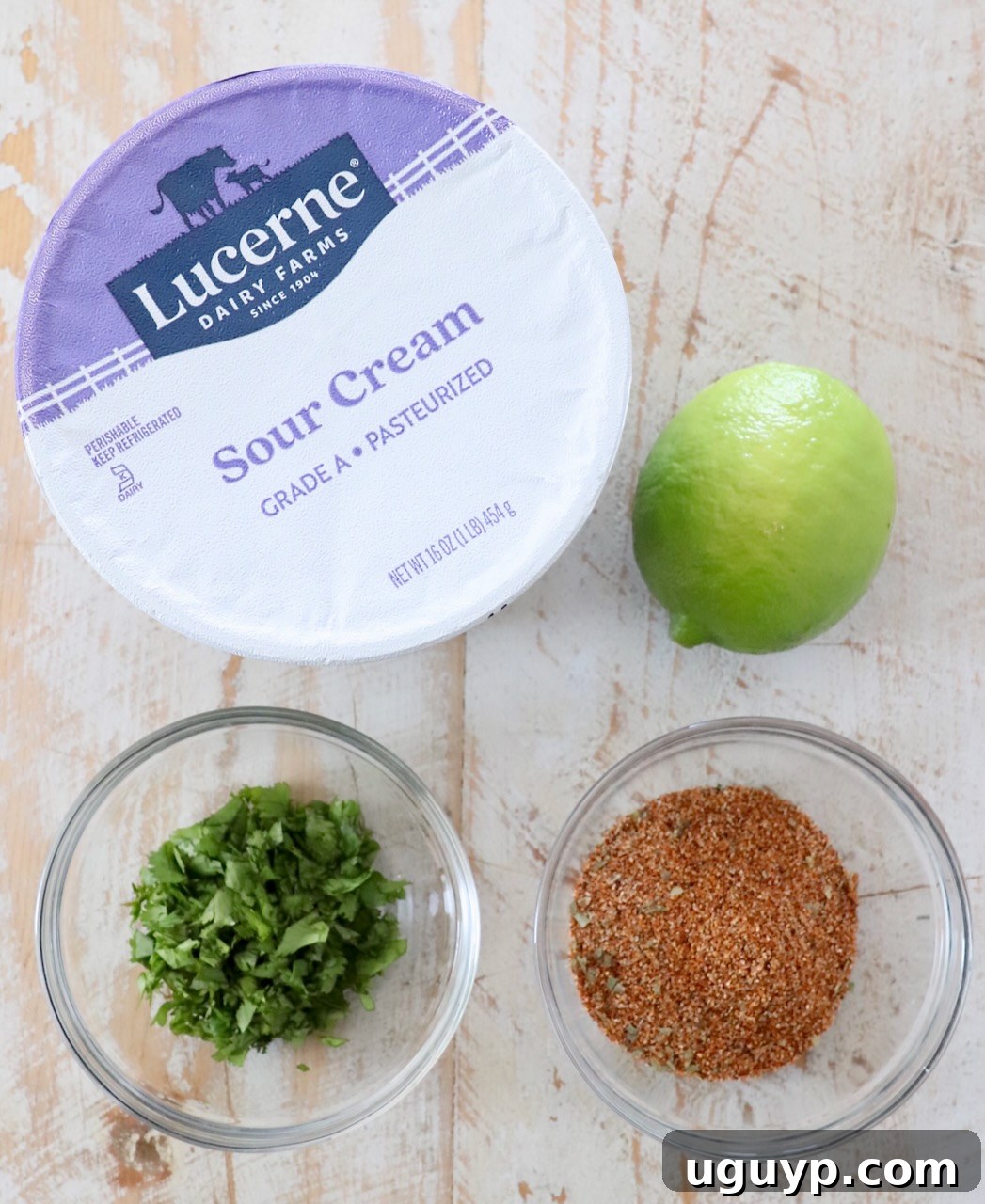 Ingredients for creamy Southwest Salad Dressing laid out on a white wooden board, including sour cream, lime, cilantro, and spices.
