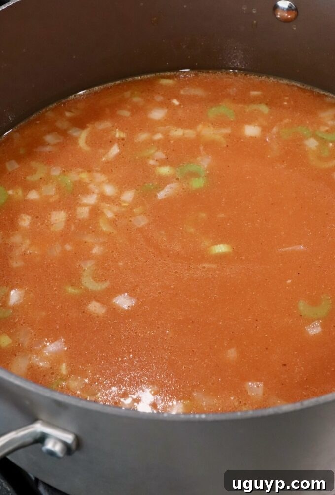 Seasoned chicken broth with diced vegetables simmering in a pot.