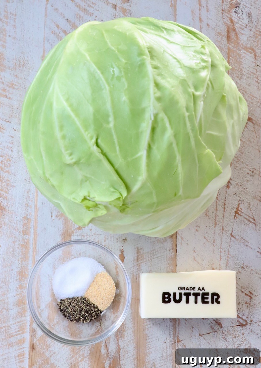 Fresh ingredients for steaming cabbage, including a whole head of green cabbage, butter, salt, pepper, and garlic powder, arranged on a rustic white wooden board.