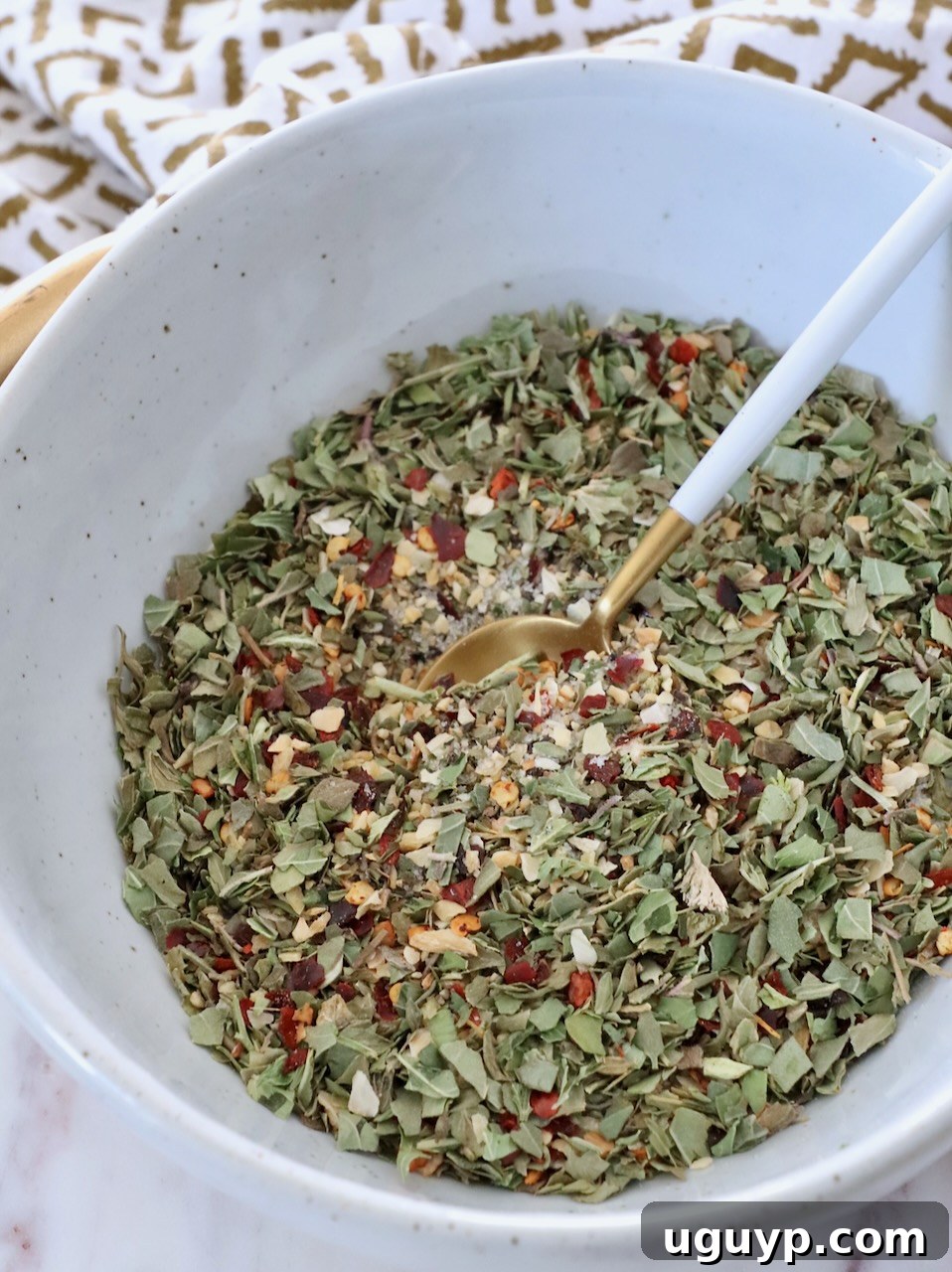 A bowl filled with a homemade blend of Italian herbs and spices, with a small spoon resting in it.