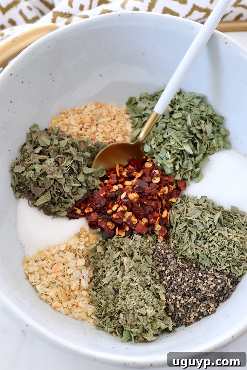A bowl sectioned with various Italian herbs and spices, with a small spoon in one section, highlighting the individual components.
