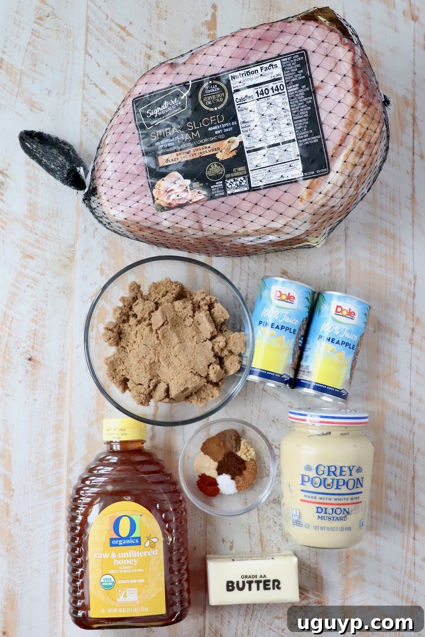 ingredients for honey baked ham laid out on a white wood board, including ham, pineapple juice, honey, butter, dijon mustard, brown sugar, and various spices