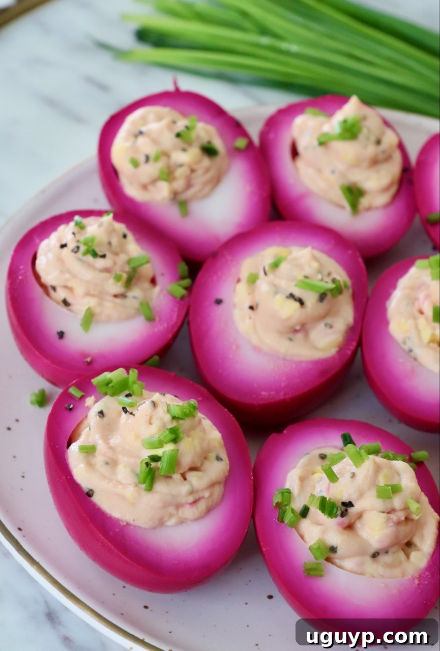 Vibrant pink beet pickled deviled eggs garnished with fresh chives on a white plate