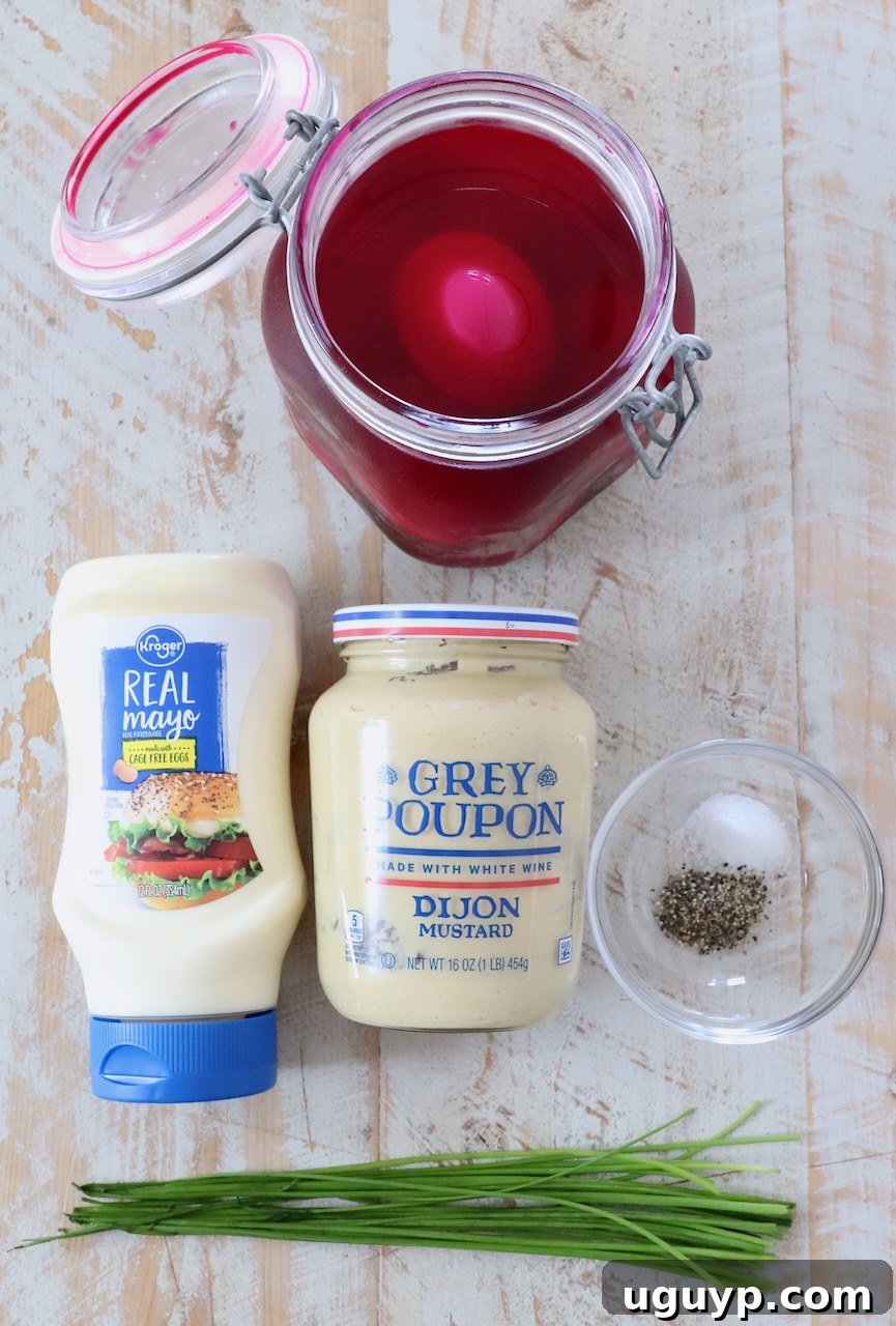 Ingredients for beet deviled eggs laid out on a white wooden board, including hard boiled eggs, mayonnaise, dijon mustard, and chives