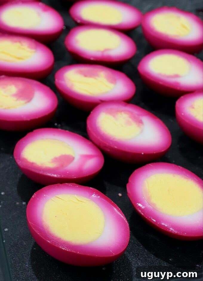 Beet-pickled hard boiled eggs, now pink, sliced in half on a cutting board, revealing the vibrant color