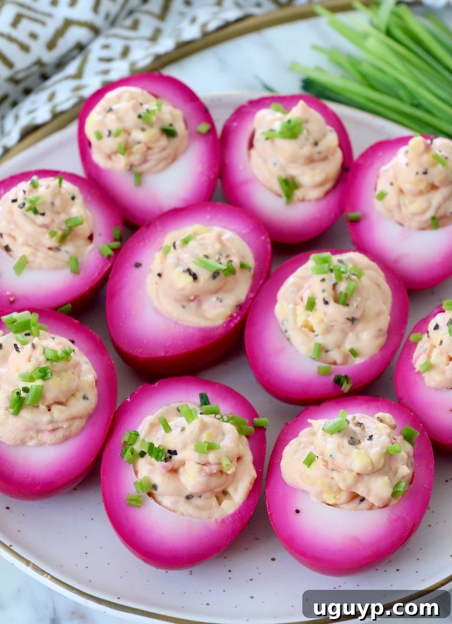 Platter of bright pink beet deviled eggs, garnished with chives, ready to be served